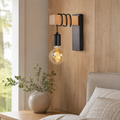 Black wood and metal exposed bulb wall sconce beside a bed.