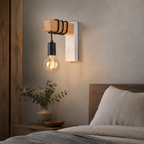 White wood and metal exposed bulb wall sconce beside a bed.