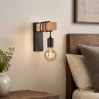 Black wood and metal exposed bulb wall sconce near a headboard.