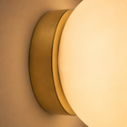 Close-up shows the gold-tone mount and glowing edge of the round wall sconce.