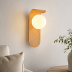 Light wood wall sconce with frosted globe glowing above a bedside table.