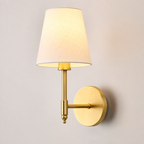 Gold wall sconce with white fabric shade displayed against a neutral background.