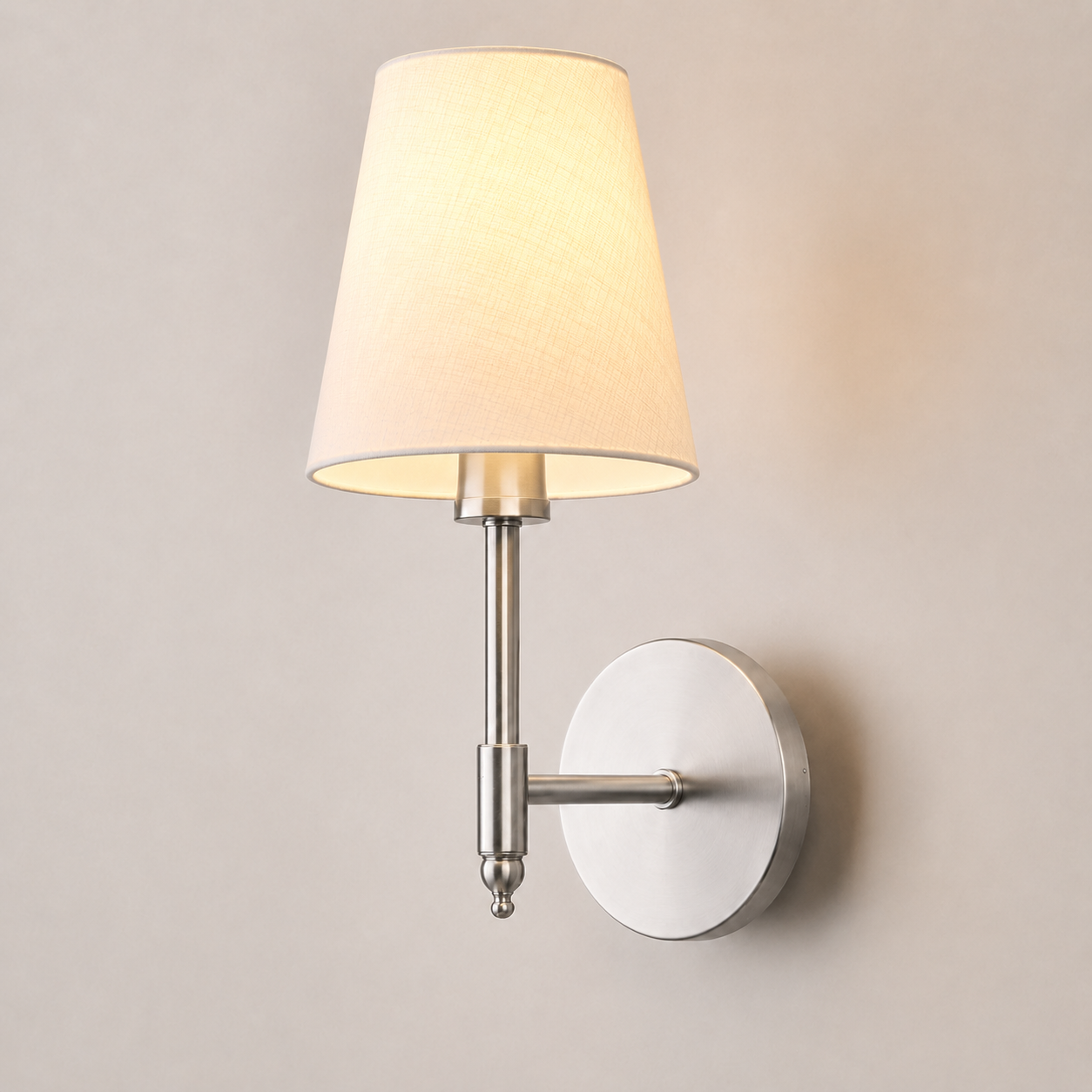 Silver wall sconce with a white fabric shade, illuminated against a neutral wall.
