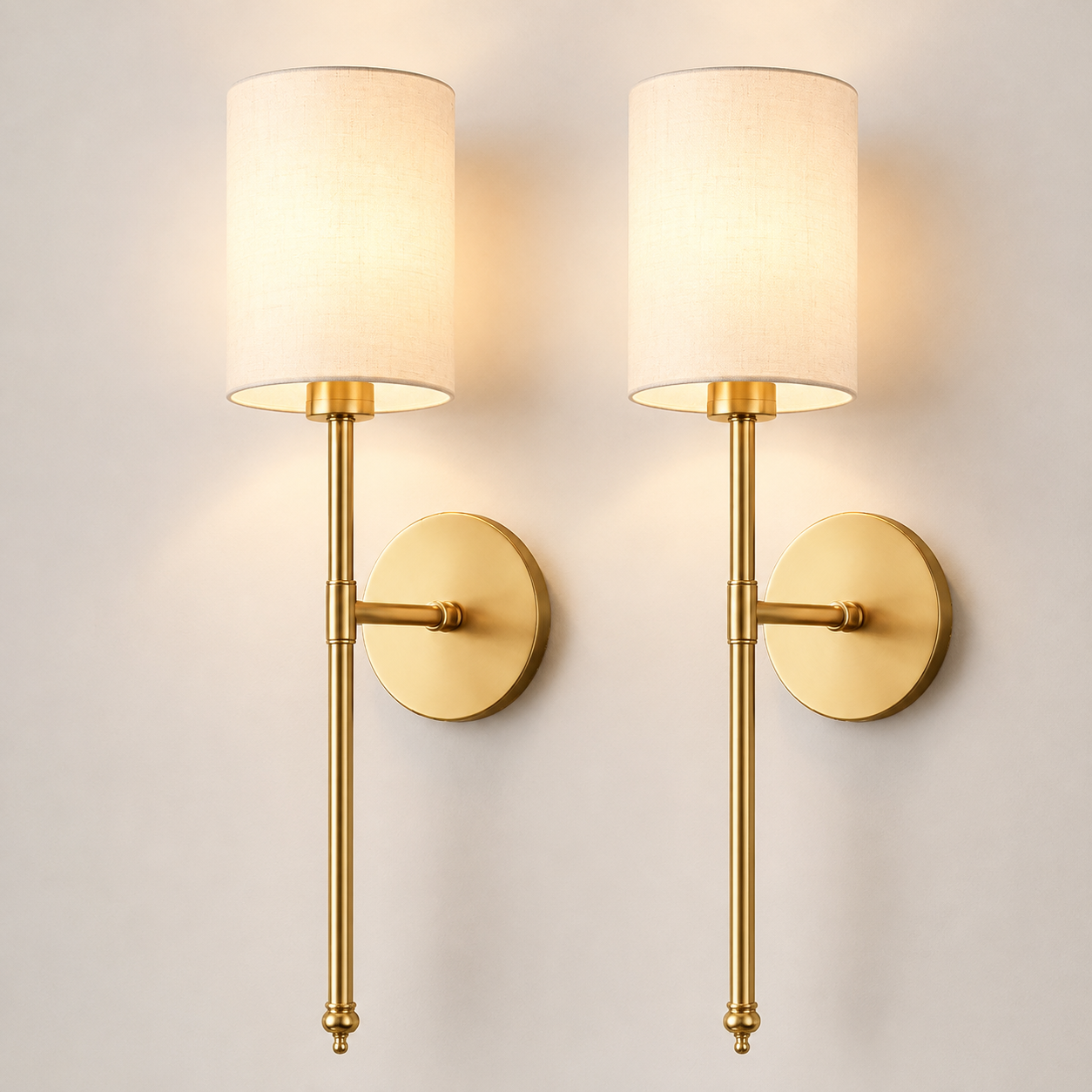 Set of two gold wall sconces with tall cylindrical white shades on a plain background.