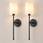 Pair of black wall sconces with white fabric shades, illuminated against a neutral wall.