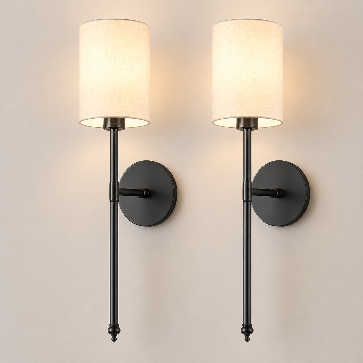 Pair of black wall sconces with white fabric shades, illuminated against a neutral wall.