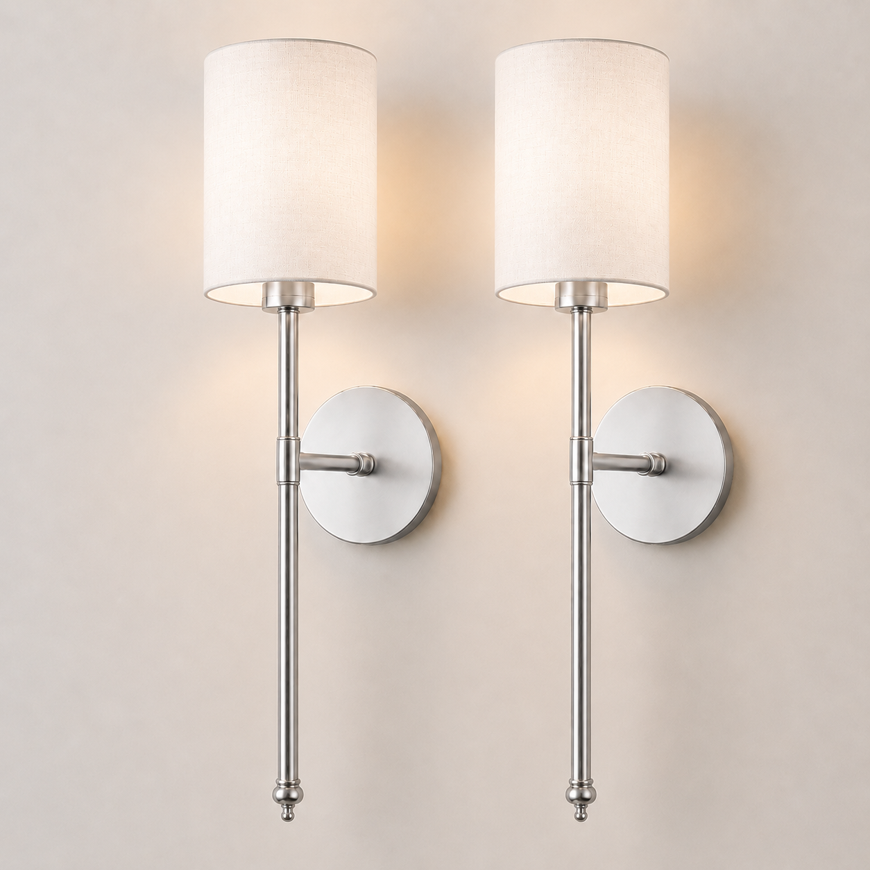 Pair of silver wall sconces with white fabric shades, illuminated against a neutral wall.