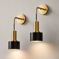 Pair of gold wall sconces with black cylindrical shades, illuminated against a neutral wall.