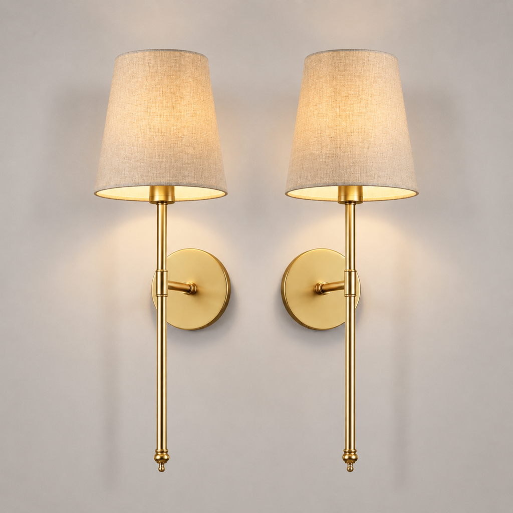 Set of two gold wall sconces with tapered neutral shades centered on a plain background.