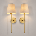 Set of two gold wall sconces with tapered neutral shades centered on a plain background.
