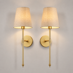 Set of two gold wall sconces with tapered neutral shades centered on a plain background.