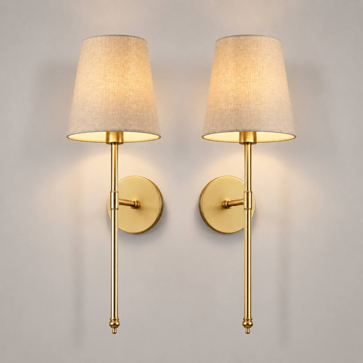Set of two gold wall sconces with tapered neutral shades centered on a plain background.