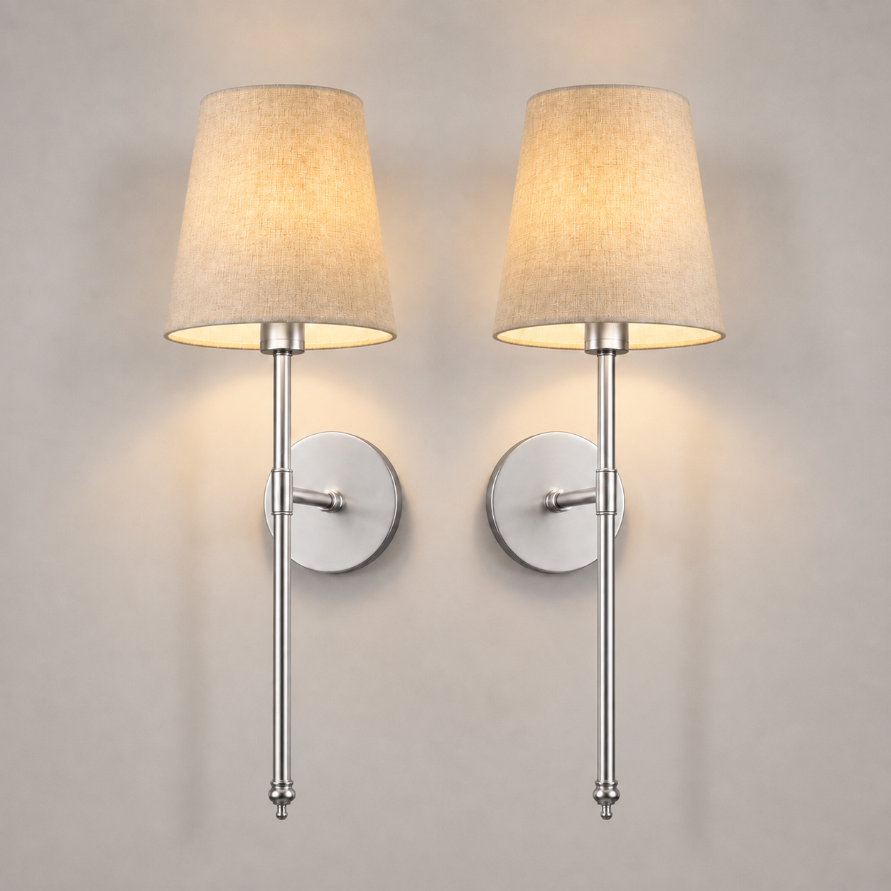 Pair of silver wall sconces with white fabric shades, illuminated against a neutral wall.