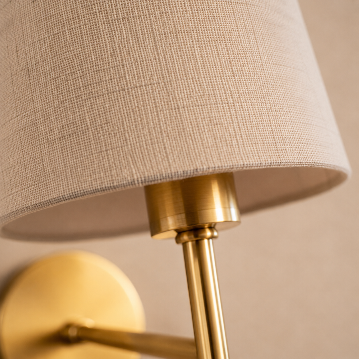 Close-up of a wall sconce showing the round mounting plate, slender arm, and tapered shade.