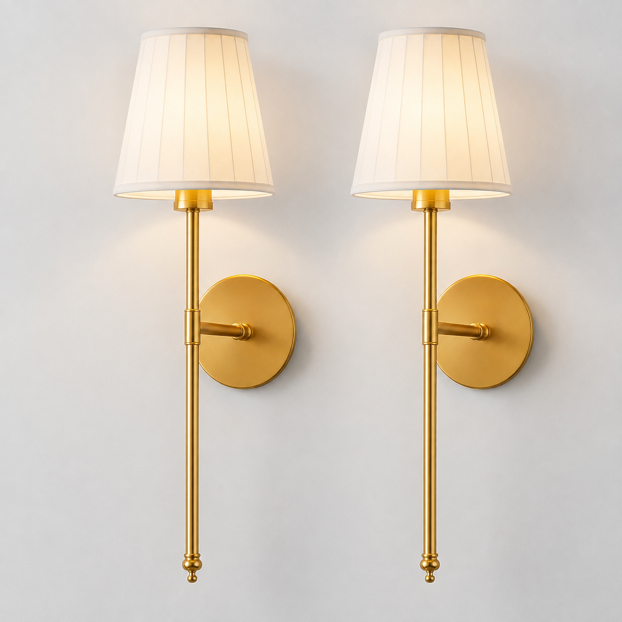 Pair of gold wall sconces with white pleated fabric shades illuminated against a neutral wall.