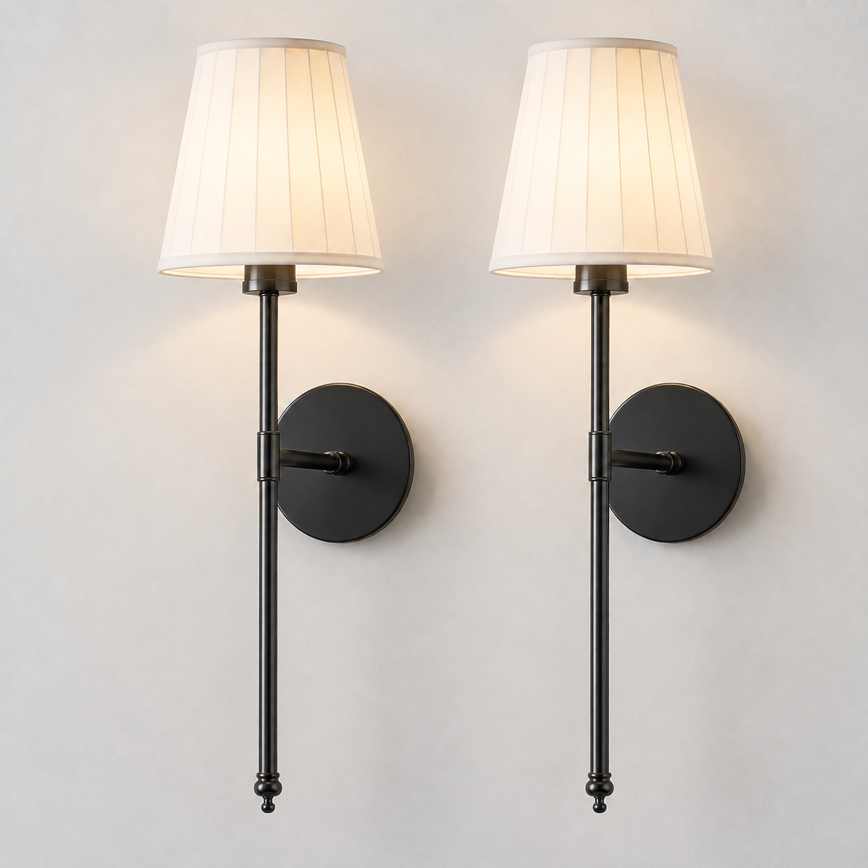 Pair of black wall sconces with white pleated shades illuminated against a neutral wall.