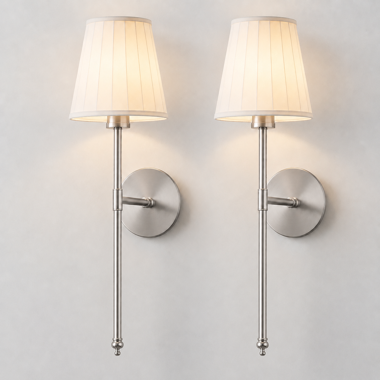 Pair of silver wall sconces with white pleated shades illuminated against a neutral wall.