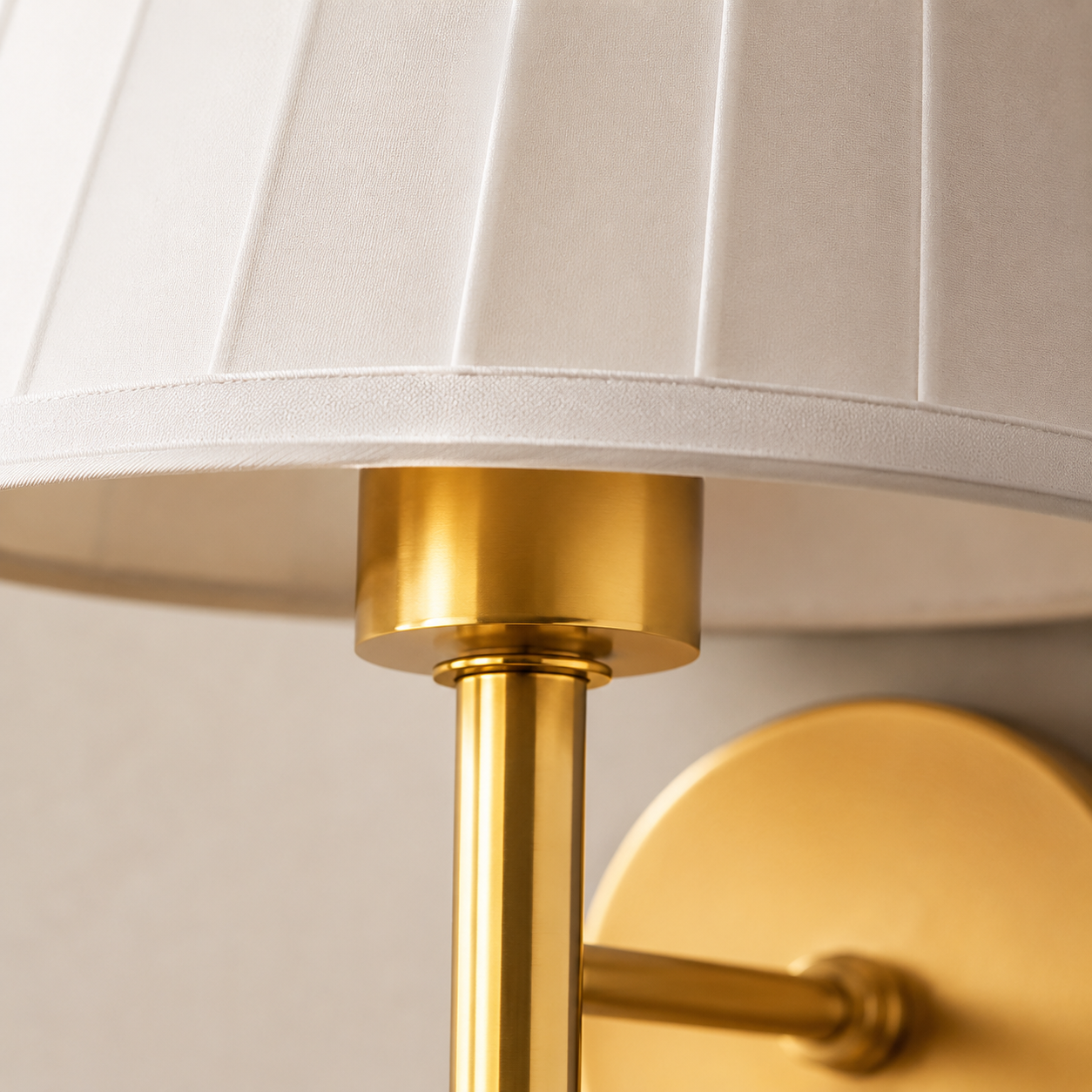 Close-up of a white pleated fabric shade and gold wall sconce frame.