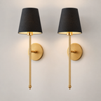 Pair of gold wall sconces with black fabric shades illuminated against a neutral wall.