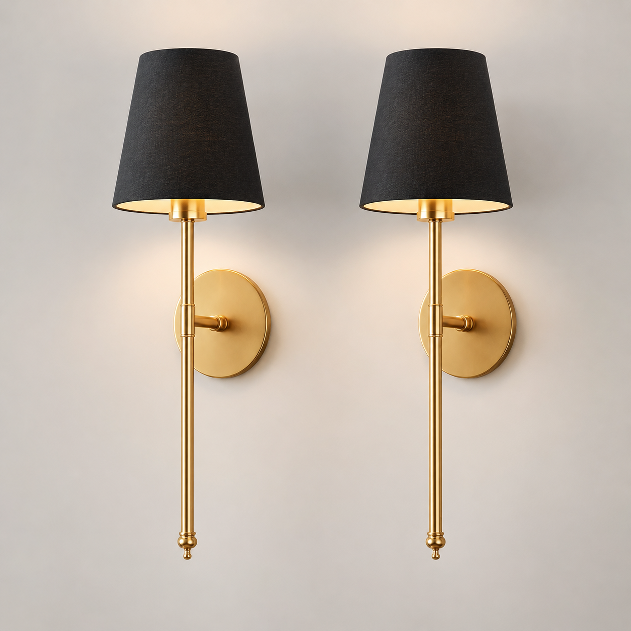 Pair of gold wall sconces with black fabric shades illuminated against a neutral wall.