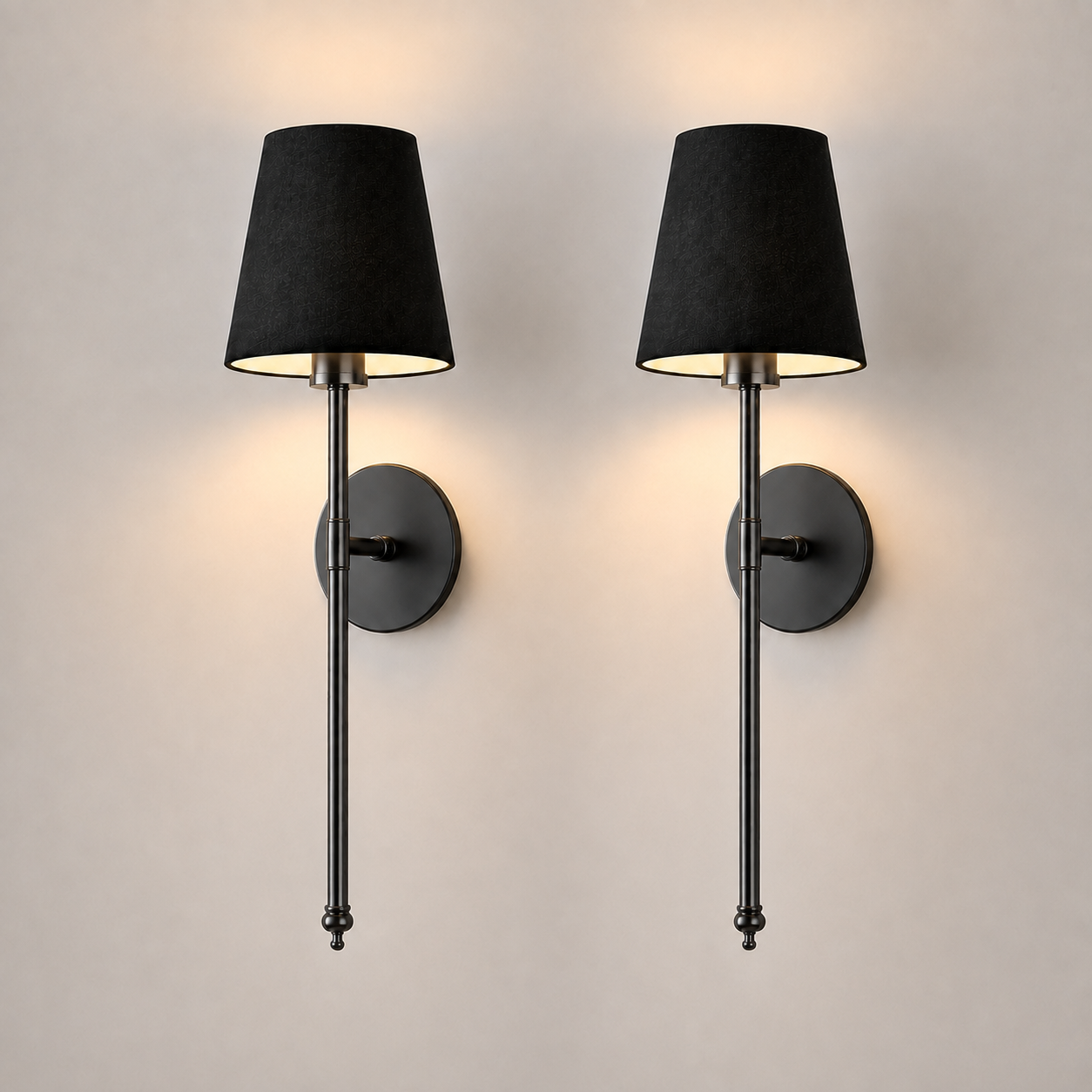 Pair of black wall sconces with black fabric shades illuminated against a neutral wall.