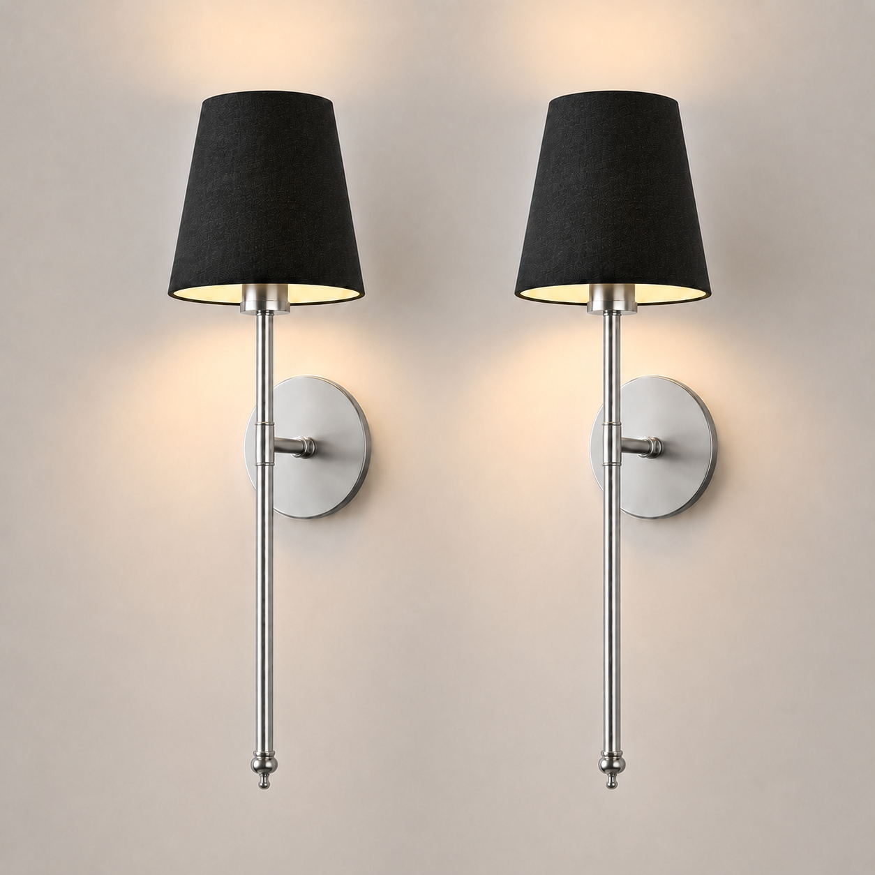 Pair of silver wall sconces with black fabric shades illuminated against a neutral wall.
