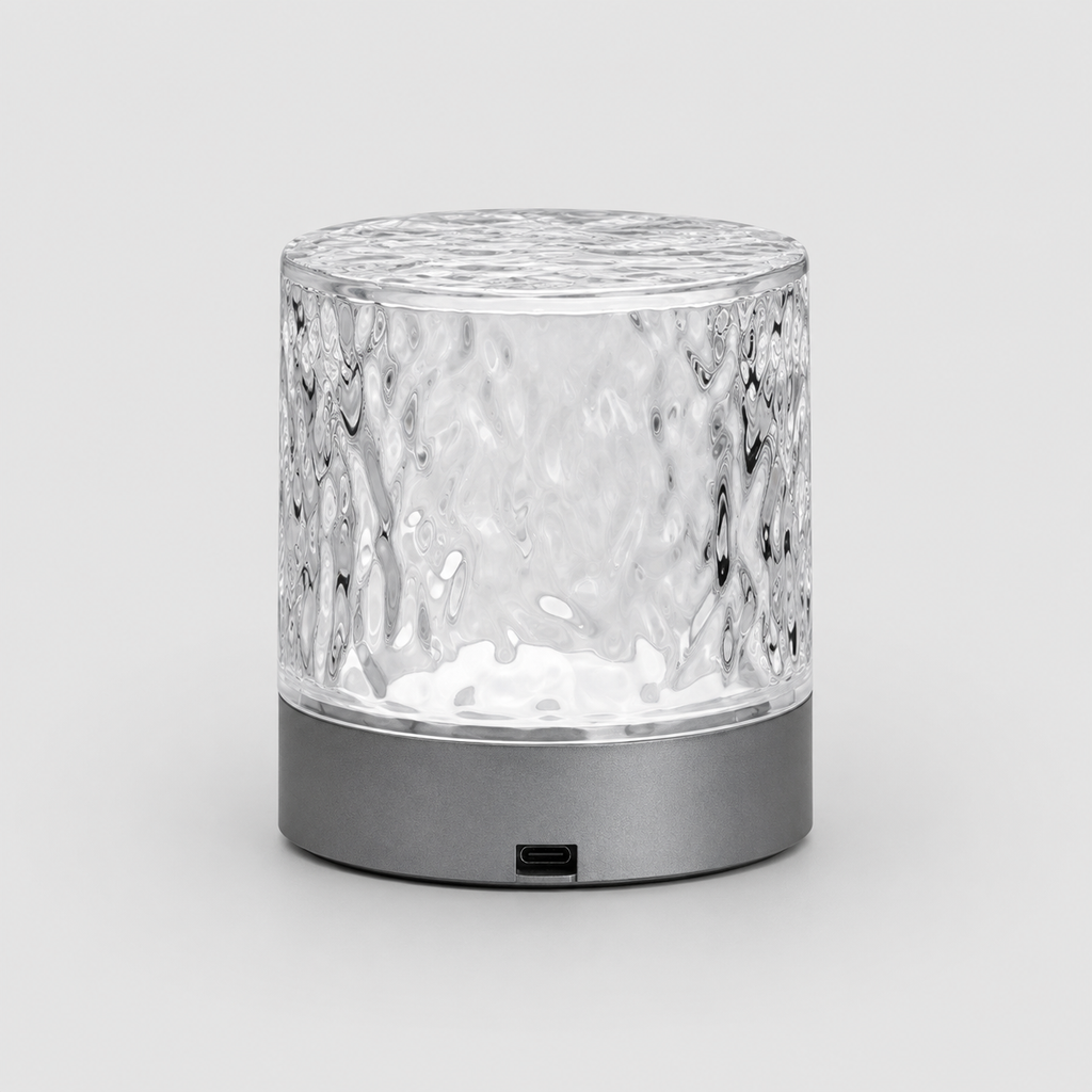 A modern cylindrical table lamp with a textured, hammered clear glass shade and a matte dark gray base, shown on a light gray background.