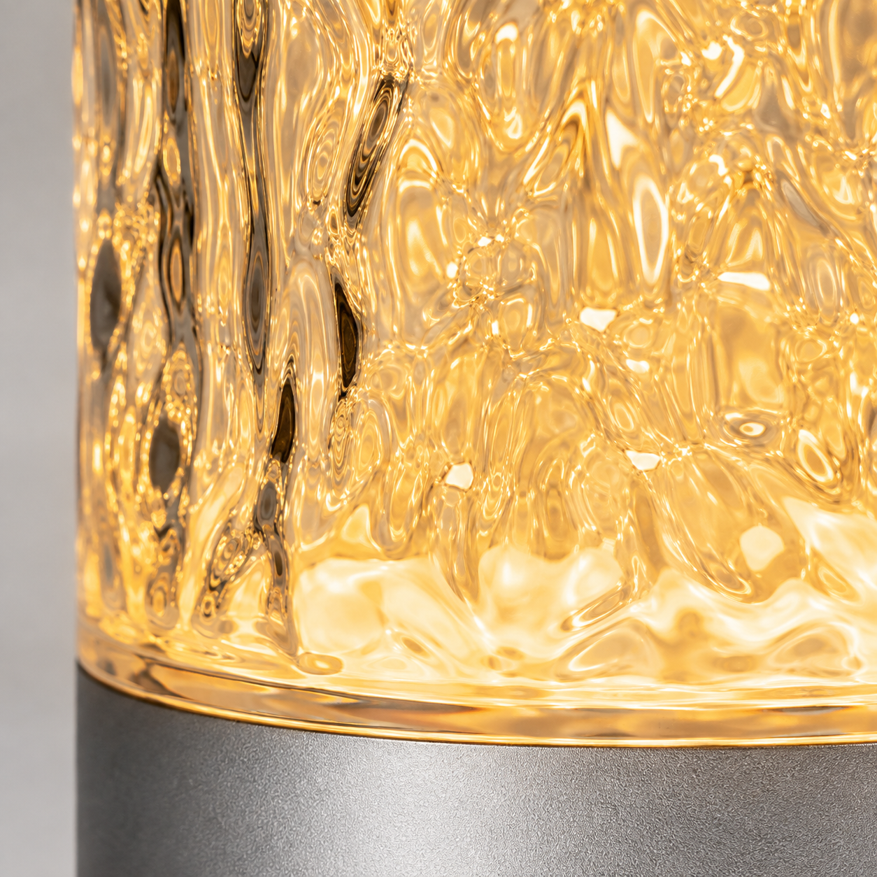 Close-up of a textured glass lamp glowing with warm amber light, showing the faceted pattern and a metallic gray base.