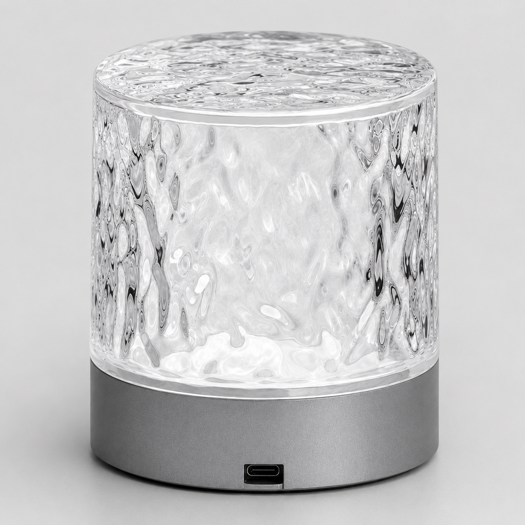 A modern cylindrical table lamp with a textured, hammered clear glass upper body and a matte dark gray metallic base, shown on a neutral light gray background.