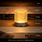 A cylindrical textured lamp with a warm glowing light, shown centered on a woven surface with horizontal material labels including Oak, Marble, Glass, Rattan, Painted Wood, and Linen. Text at the bottom reads 'FITS ANY SURFACE PERFECTLY.