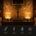 Two glowing cylindrical crystal-texture night lights on a wooden bedside table, casting a warm rippled light pattern on the wall behind them. A vase and books sit between the lights.