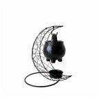 Moon shaped iron stand and hanging black cauldron against a white background.