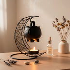 Black cauldron warmer above a tealight beside a vase and oil bottle.