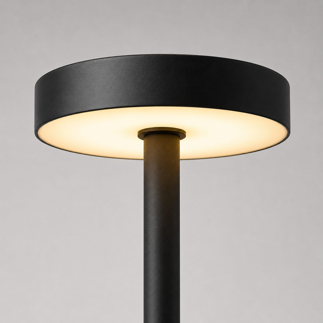 A modern black floor lamp with a wide circular shade and a slim central stem, shown lit against a neutral gray background.