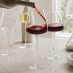 Wine glasses arranged as red wine is poured into a broad crystal bowl