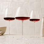 Wine glasses trio filled with red wine against a softly lit white tile wall