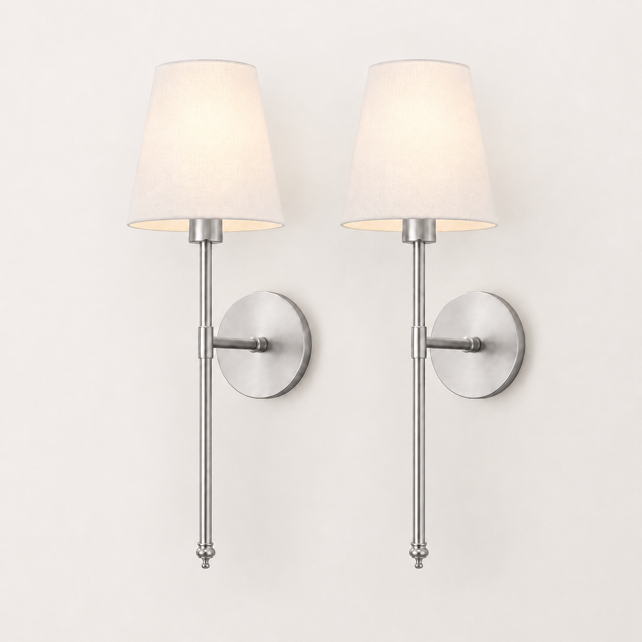 Two matching wall sconces with tapered off-white fabric shades and brushed silver metal arms, mounted side by side on a plain light wall.