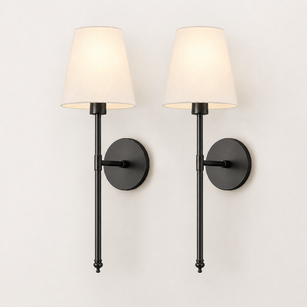 A pair of modern wall sconces with black metal fixtures and tapered off-white fabric shades, shown lit against a plain white wall.