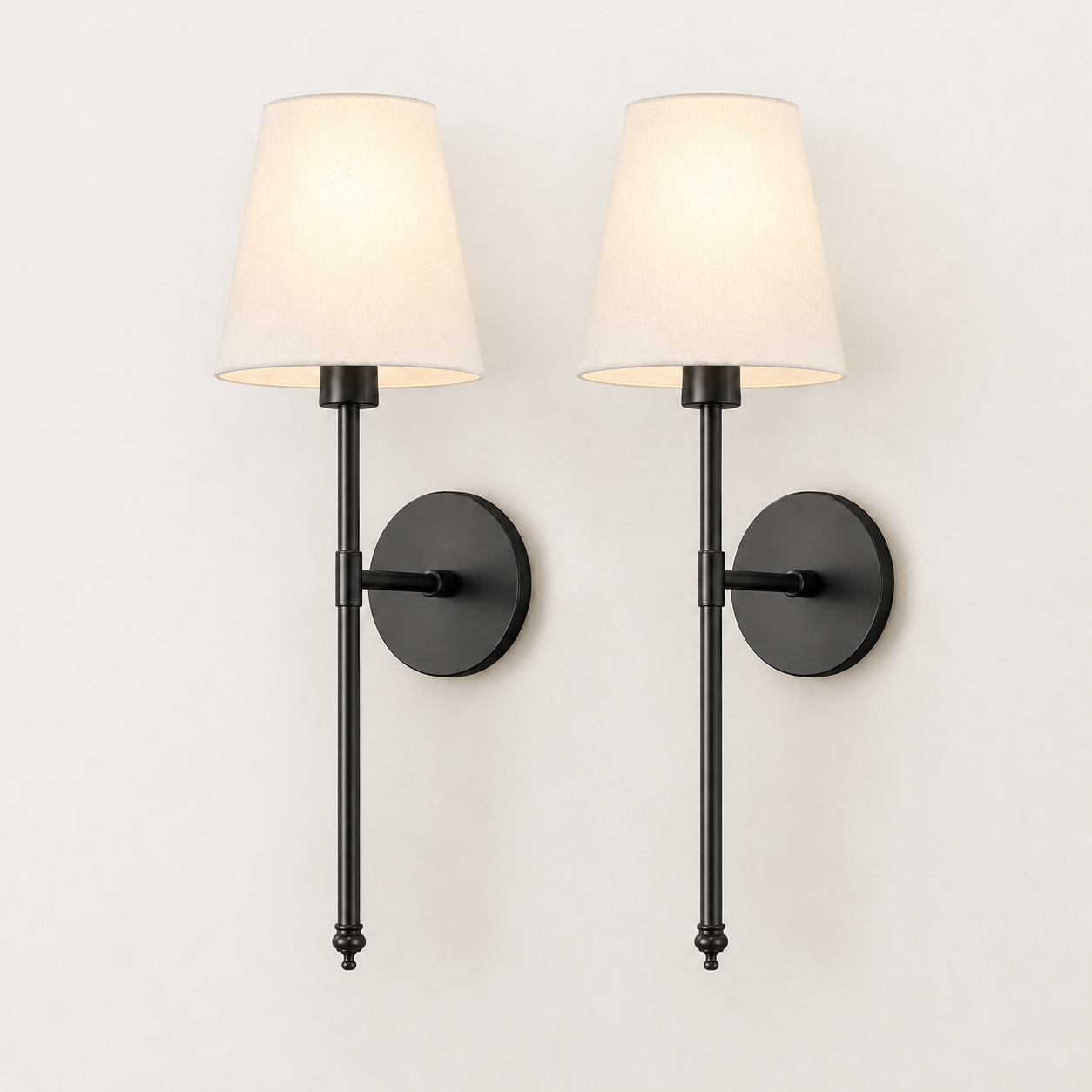 A pair of modern wall sconces with black metal fixtures and tapered off-white fabric shades, shown lit against a plain white wall.
