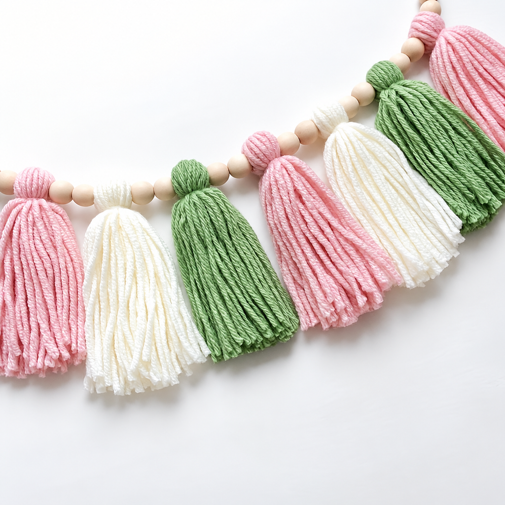 Wooden bead tassel garland close-up showing green, pink and white yarn texture and natural beads.