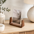 Vertical acrylic photo frame with a walnut U-shaped base on a light oak console.
