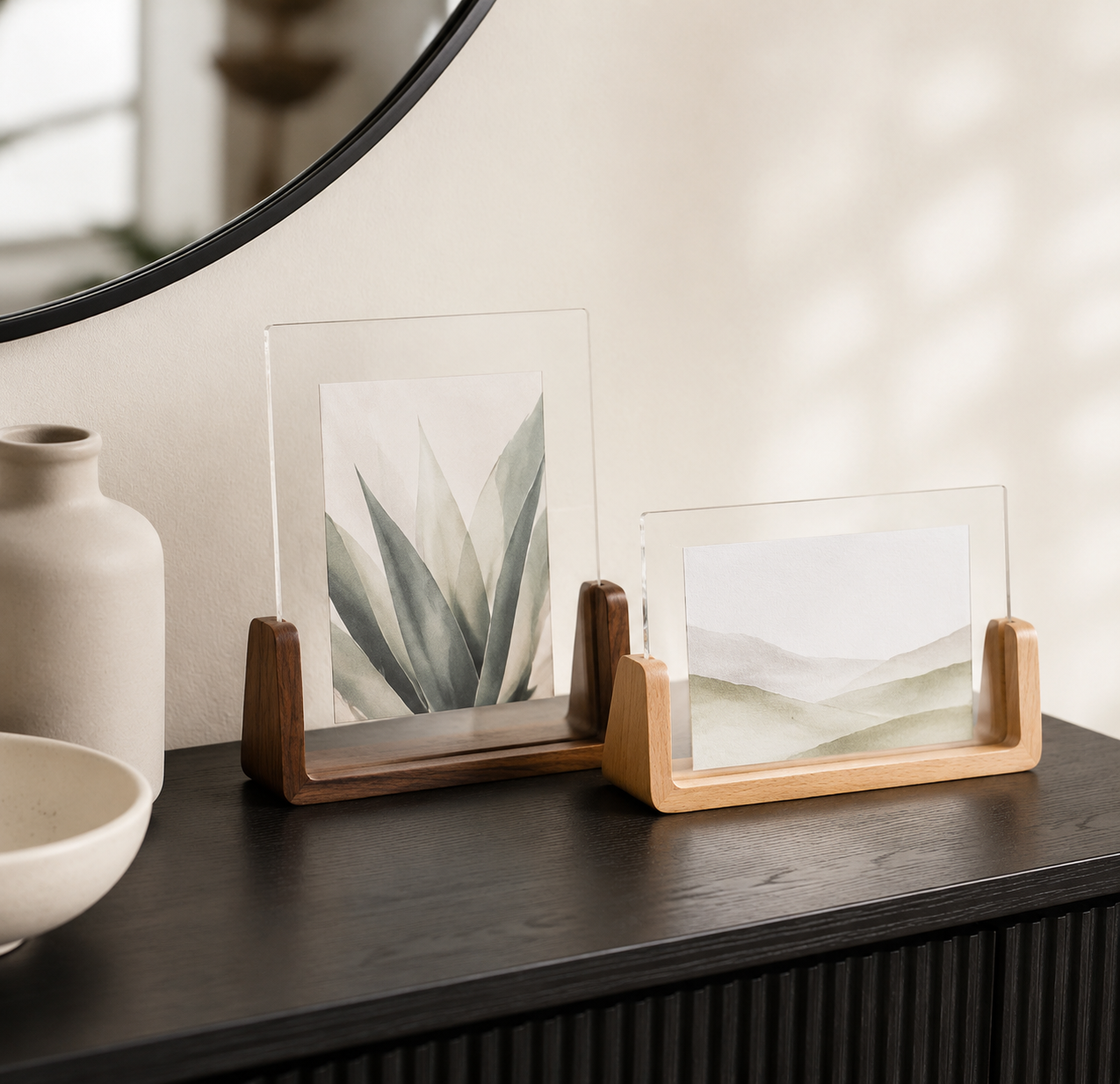Two acrylic photo frame sizes arranged below a round mirror on a dark console.
