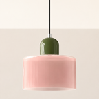 Pink circular glass pendant light with an olive cap on a warm studio wall