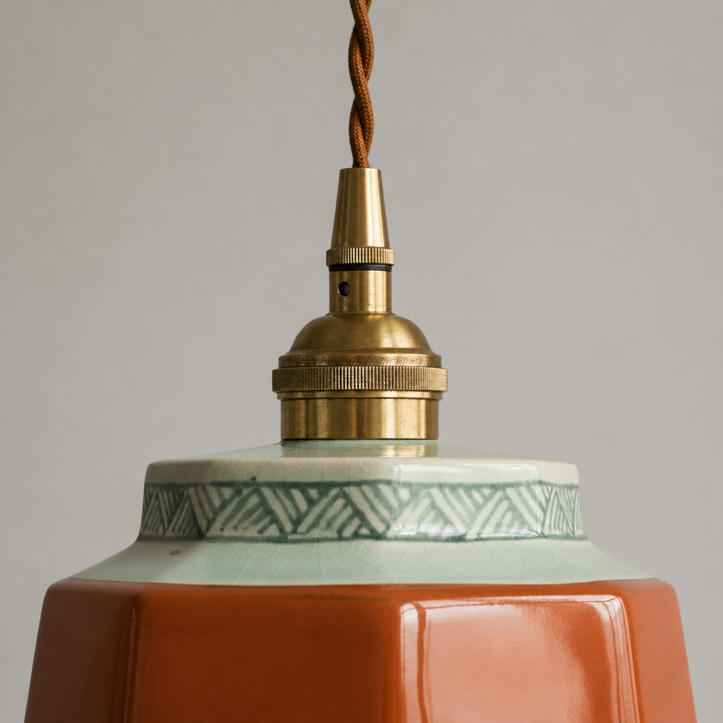 Close detail of a terracotta hand-painted ceramic pendant light with aged brass hardware