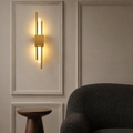 Gold dual-rod LED wall sconce glowing above a walnut pedestal table