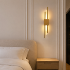 Gold dual-rod LED wall sconce beside an upholstered bedroom headboard