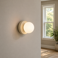 Beige Nordic glass globe wall sconce glowing beside a double-hung window on a warm gray wall