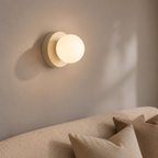 Beige Nordic glass globe wall sconce glowing above a textured cream sofa