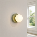 Green Nordic glass globe wall sconce glowing beside a double-hung window