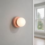 Pink Nordic glass globe wall sconce glowing on a cool-gray wall near a window